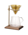 Coffee brewing setup with glass carafe and gold metal stand on a white background
