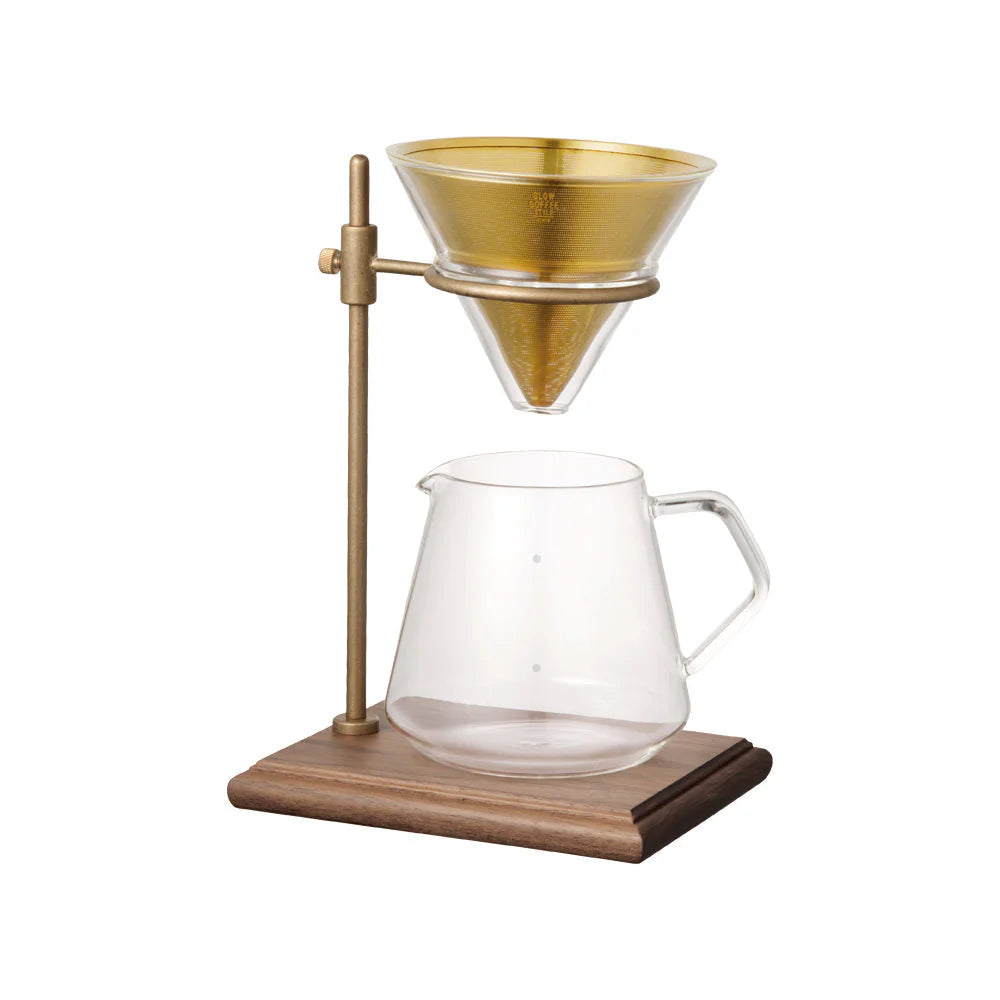 Coffee brewing setup with glass carafe and gold metal stand on a white background