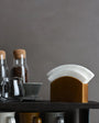 Coffee-making setup with glass jars, coffee beans, a filter, and mugs on a dark surface against a gray background.