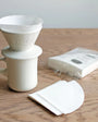 White ceramic coffee brewer with a pack of filters on a wooden surface