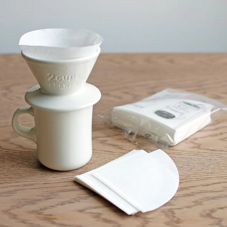 White ceramic coffee brewer with a pack of filters on a wooden surface