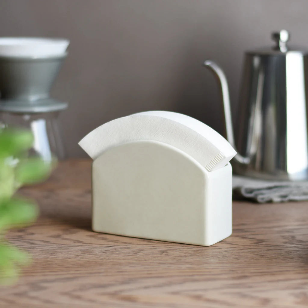 White ceramic Kinto Paper Filter Stand on a wooden surface with kitchen items in the background