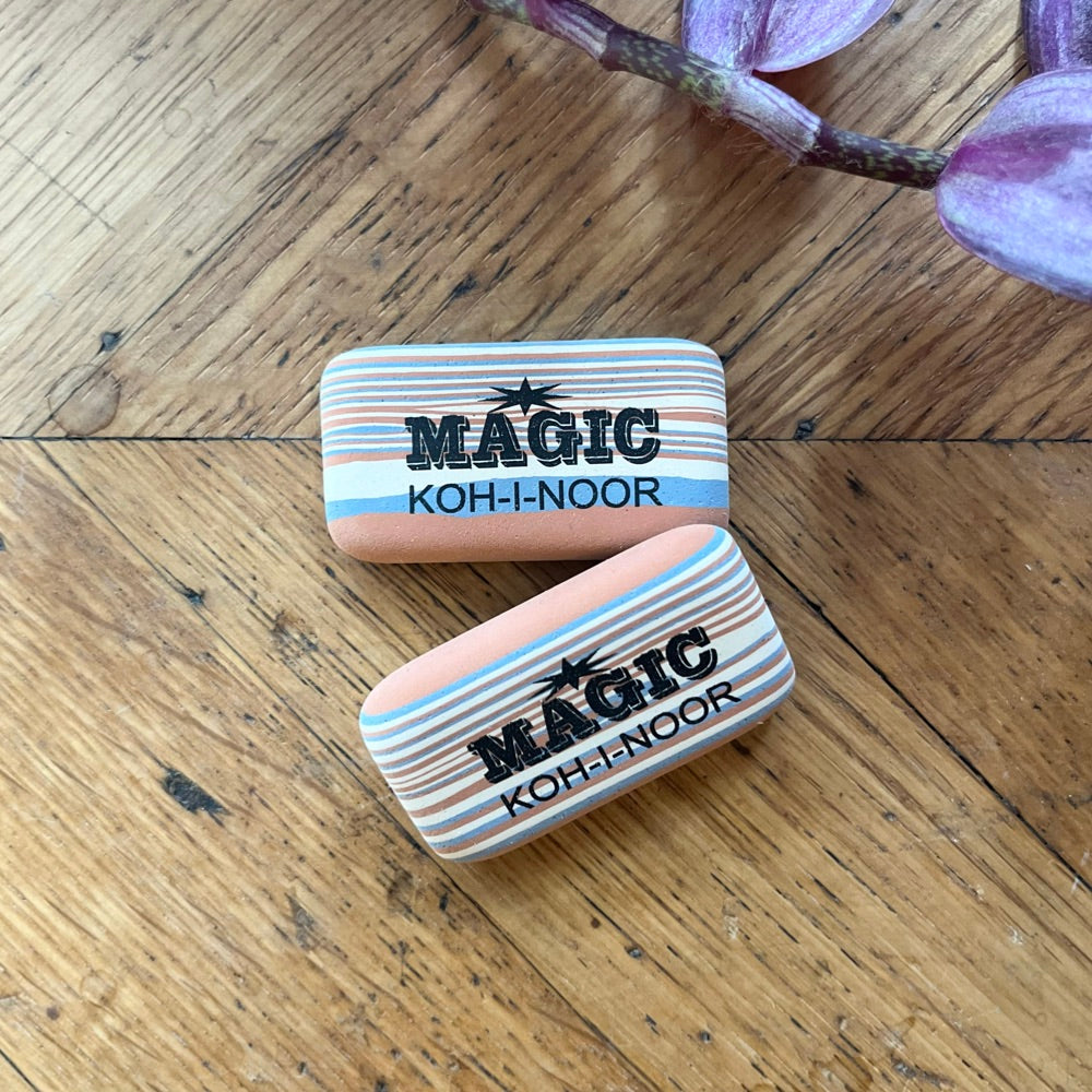 Two Magic Koh-I-Noor erasers on a wooden surface with purple flowers in the background.