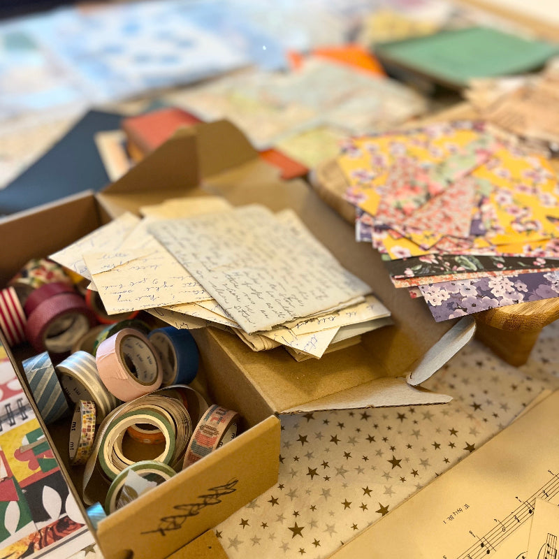 Box containing stationery items including paper, envelopes, and tape on a table.