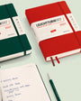Two Leuchtturm1917 notebooks, one green and one red, on a light green background with a pen.