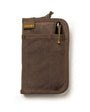 A pocket journal with a waxed canvas cover, displayed alongside a pen and cables, revealing the interior dot grid refill and organization pockets.