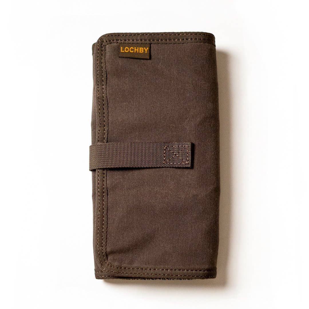 A partially unrolled tool roll with a brown waxed canvas exterior, aluminum hook fastener, and multiple pockets containing pens and other tools.