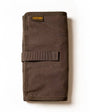 A partially unrolled tool roll with a brown waxed canvas exterior, aluminum hook fastener, and multiple pockets containing pens and other tools.