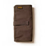A partially unrolled tool roll with a brown waxed canvas exterior, aluminum hook fastener, and multiple pockets containing pens and other tools.