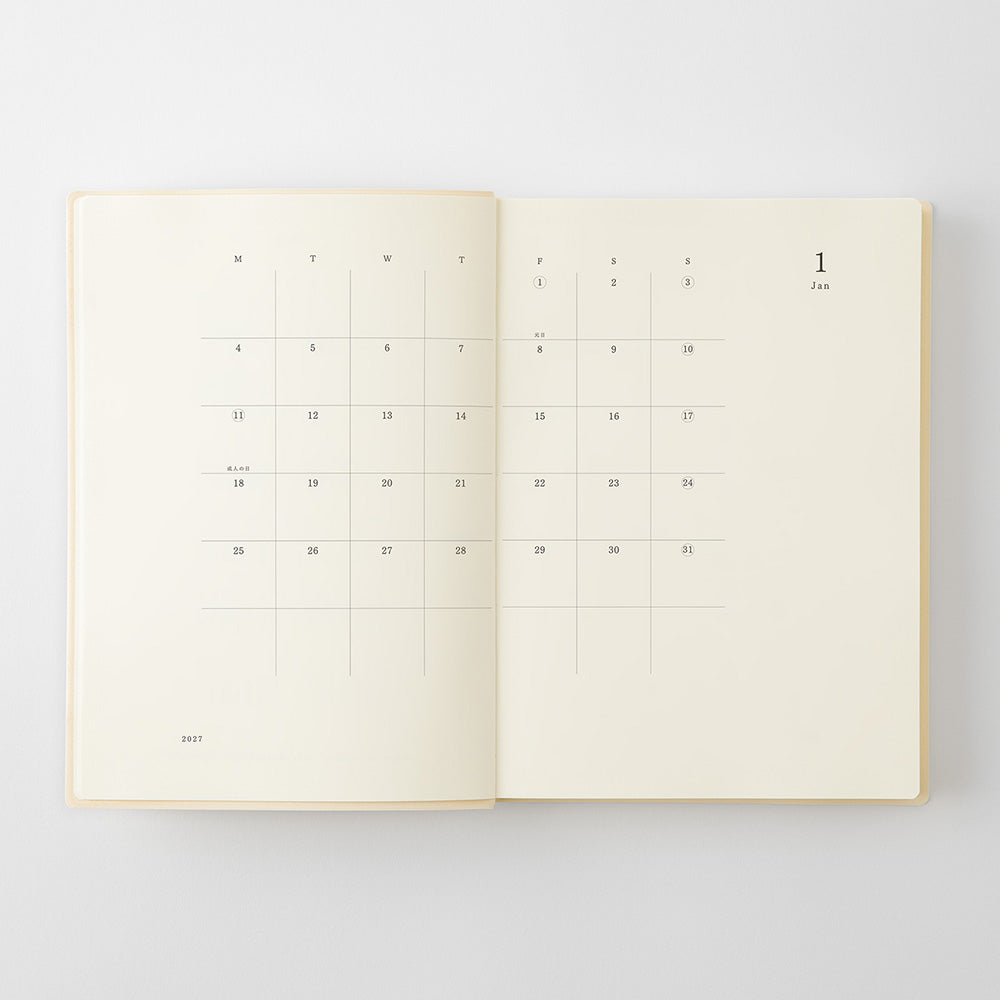 An open cream-colored planner or journal showing a minimalist monthly calendar layout on both pages, photographed from above on a light gray background.