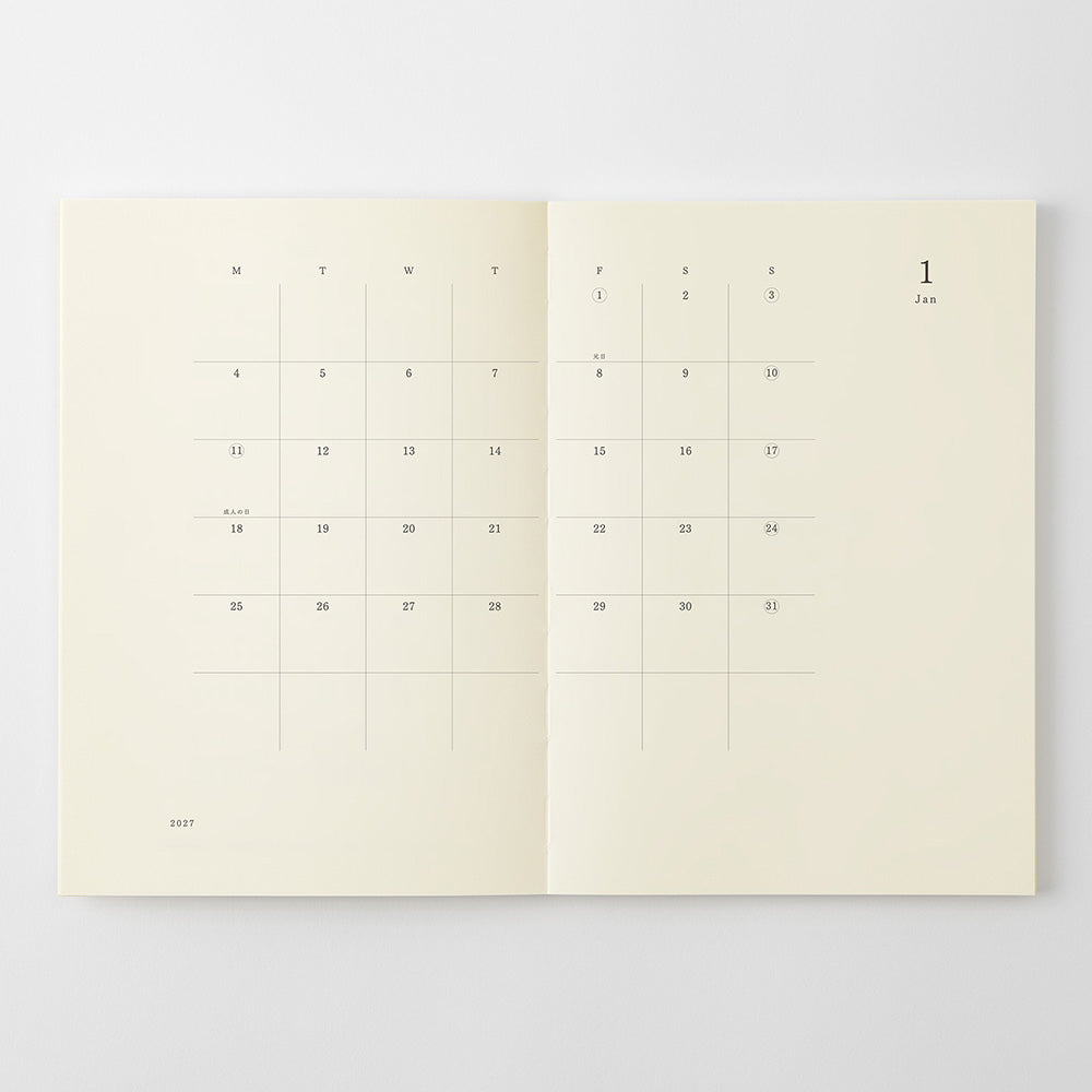 An open cream-colored planner or calendar showing minimalist monthly grids and dates on both pages, photographed against a light gray background.