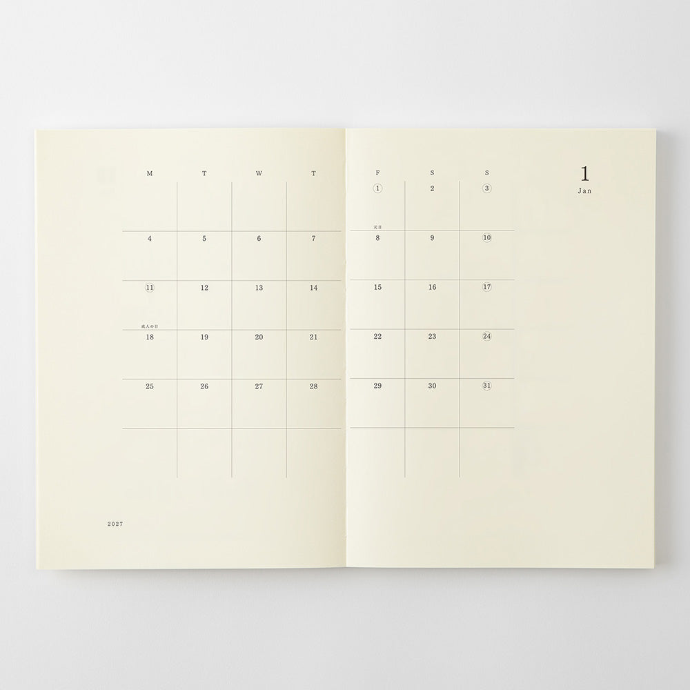 An open cream-colored planner or journal showing a minimalist monthly calendar layout on both pages, photographed against a light gray background.