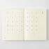 An open planner or notebook showing two cream-colored calendar pages with minimalist black grid lines and day labels, photographed against a light gray background.