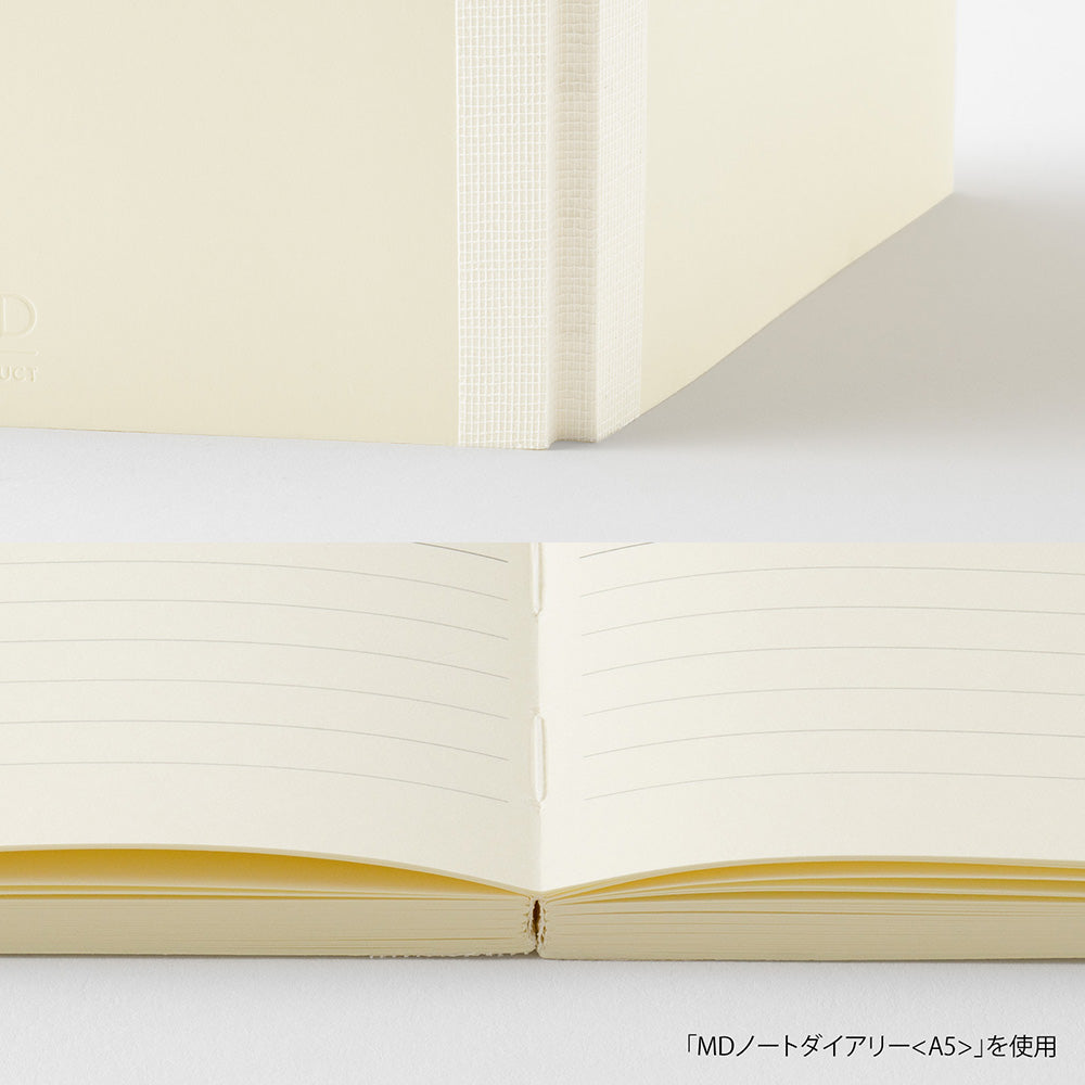 A cream-colored lined notebook shown open, with a folded view of the same notebook above it on a clean white background. Small Japanese text appears in the bottom right corner.