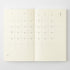 An open planner or journal showing two cream-colored interior calendar pages with minimalist black printed dates and weekday grids, photographed against a light gray background.
