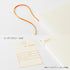 An off-white 21-day diary with a textured cover, featuring an orange elastic loop handle, a matching orange-and-cream library card insert, and Japanese text overlays describing the index seal and notebook compatibility.