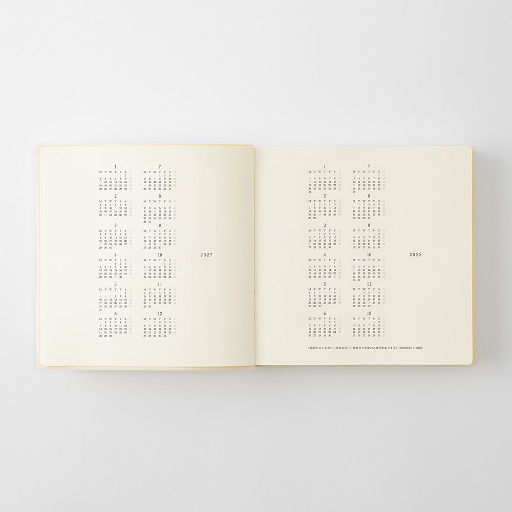 An open cream-colored book or journal showing printed calendar grids on both pages, photographed against a light gray background.