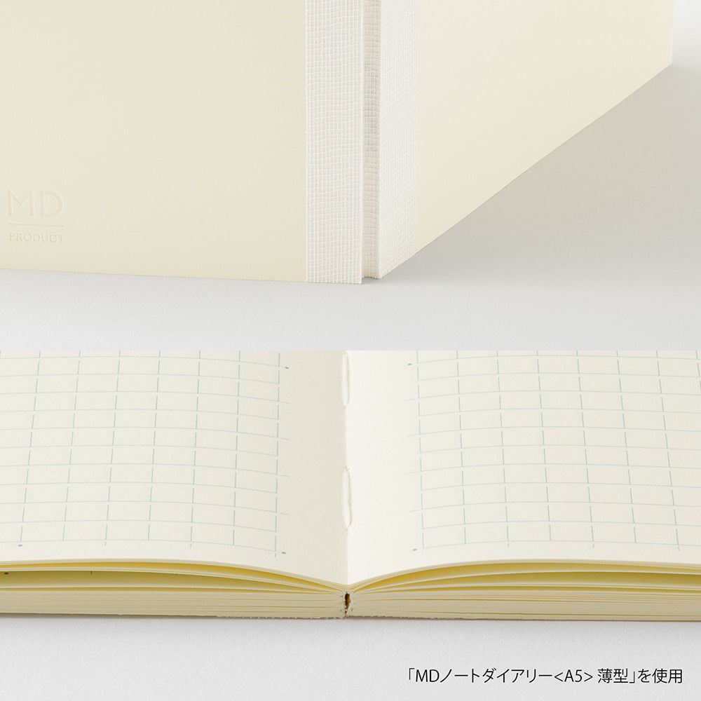 An open cream-colored grid notebook showing its double-page spread, with a matching closed notebook standing behind it on a white surface. Japanese text appears at the bottom right.
