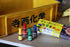 Four small bottles with colorful caps and a box on a wooden surface with a yellow sign in the background.