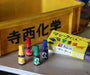 Four small bottles with colorful caps and a box on a wooden surface with a yellow sign in the background.