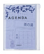 A clear plastic zippered agenda case with a light blue and white illustrated cover featuring Japanese text and a building line drawing. The word 'AGENDA' is printed across the front.