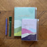 Two agendas with colorful covers on a wooden surface, accompanied by a pen and ruler.