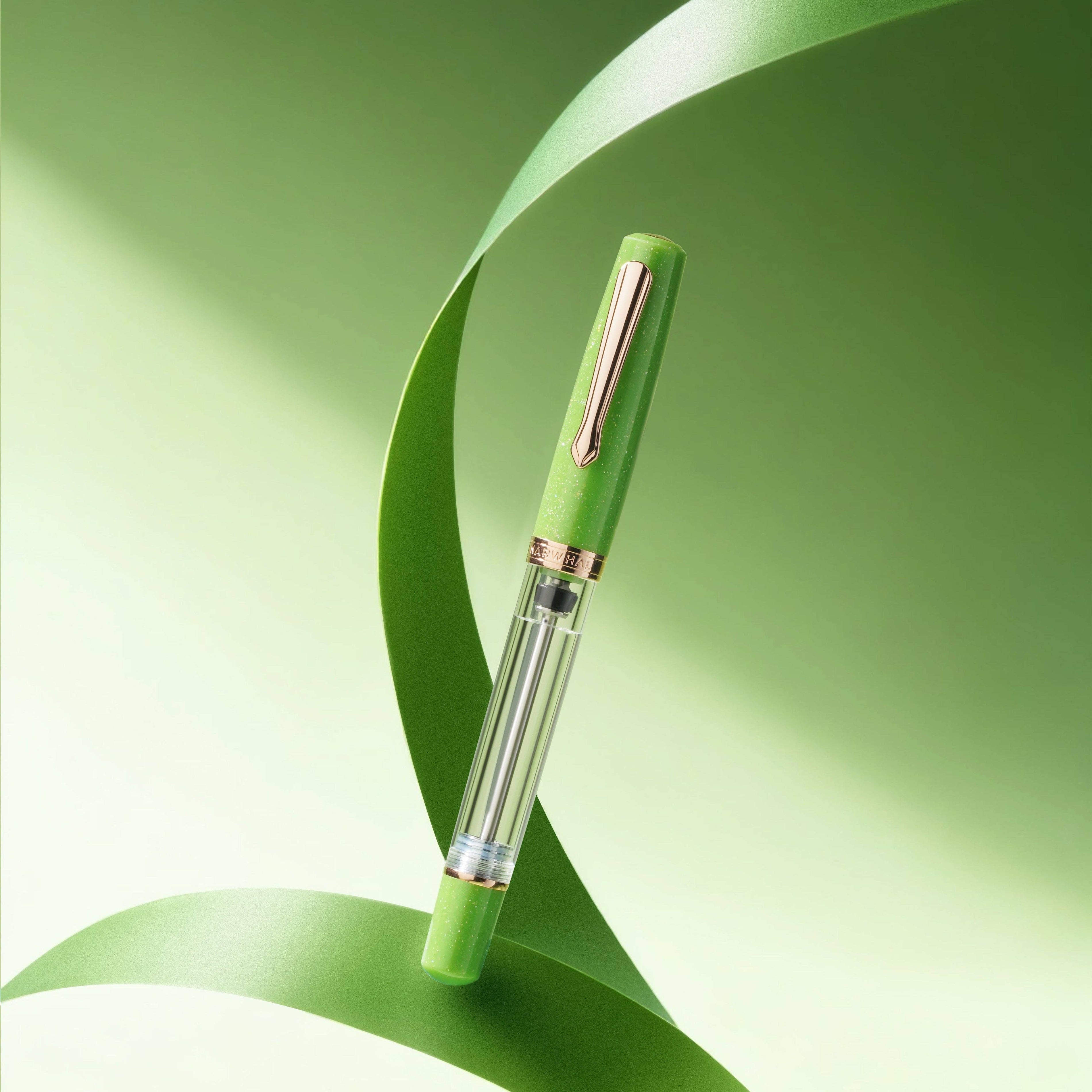 A green fountain pen with a clear barrel and rose gold accents, resting on a stylized green ribbon against a soft green gradient background.