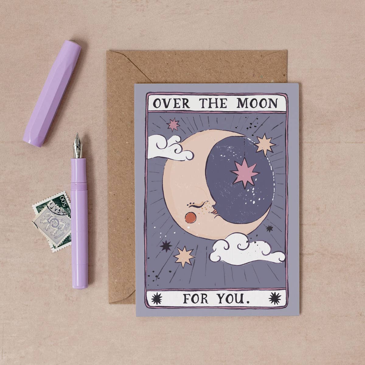 Greeting card with moon design, pen, and envelope on a beige background