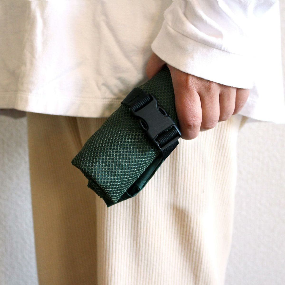 Person holding a green belt with a black buckle against a neutral background