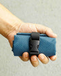 Hand holding a blue textured pouch with a black buckle against a neutral background