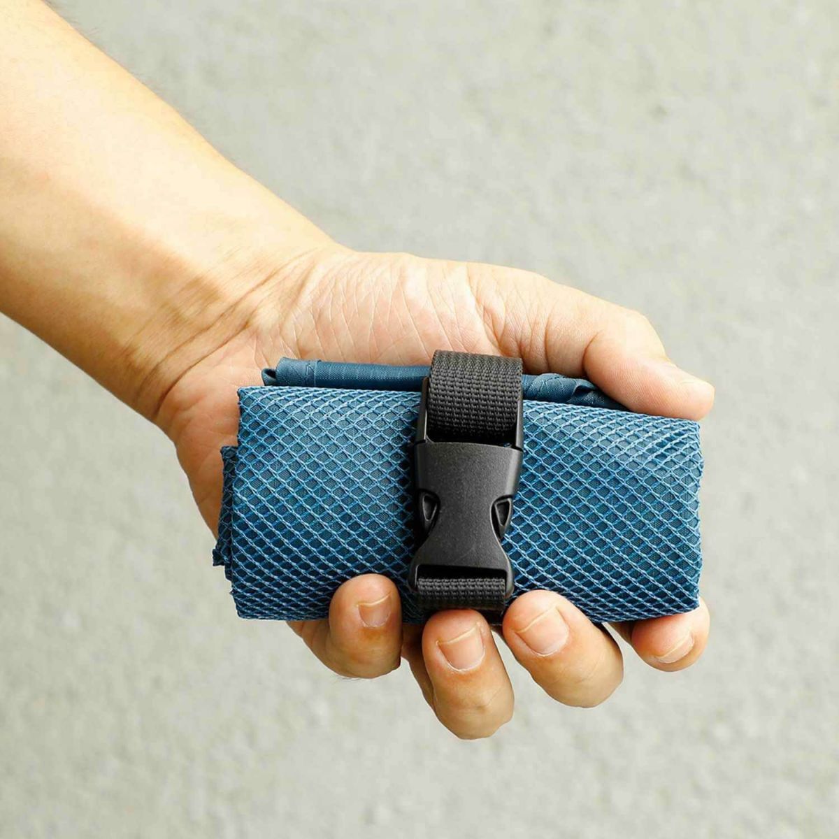 Hand holding a blue textured pouch with a black buckle against a neutral background
