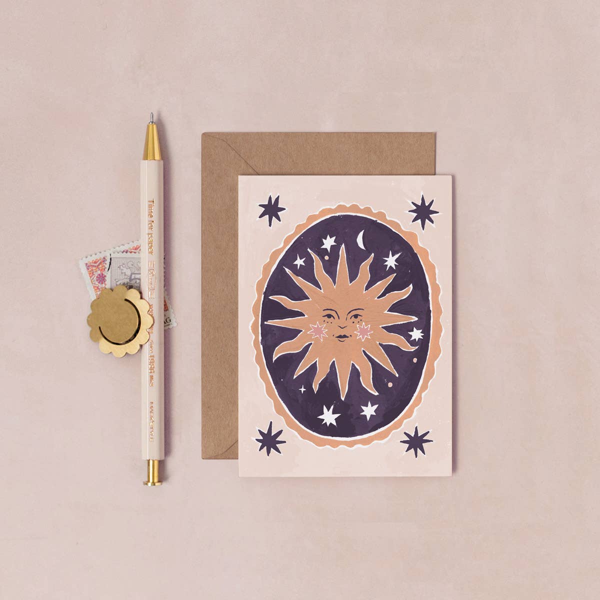 Greeting card with sun and moon design, pen, and envelope on a beige background