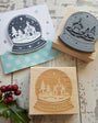 Wooden and rubber stamp with a winter scene design on a rustic wooden surface.