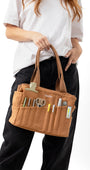 Person holding a brown tool bag with various tools on a white background