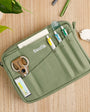 Green Scolla pencil case with stationery items on a wooden surface