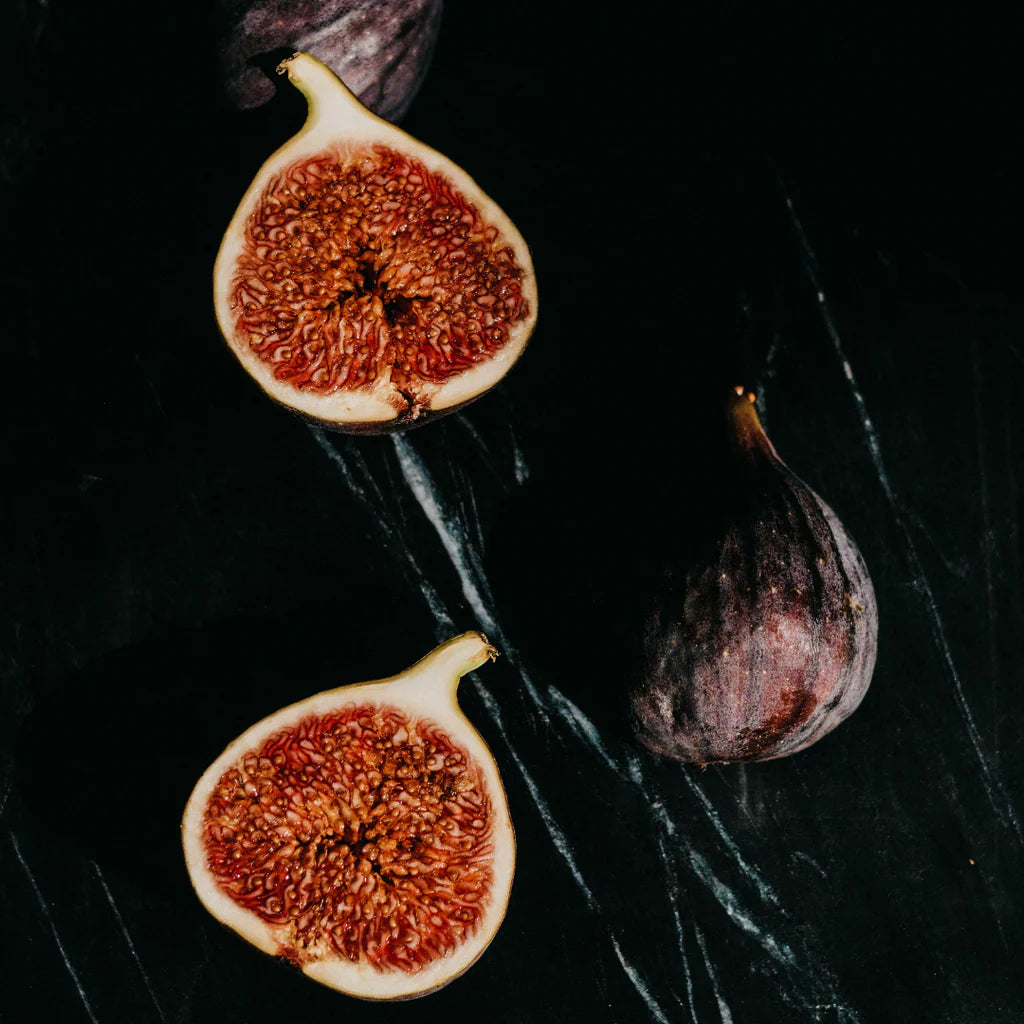 Figs, including a halved fig showing its interior, on a dark surface.