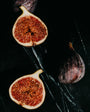 Figs, including a halved fig showing its interior, on a dark surface.