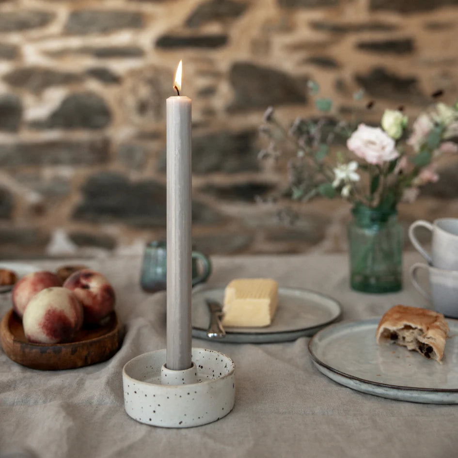 Candle in a holder on a table with food and flowers, stone wall background