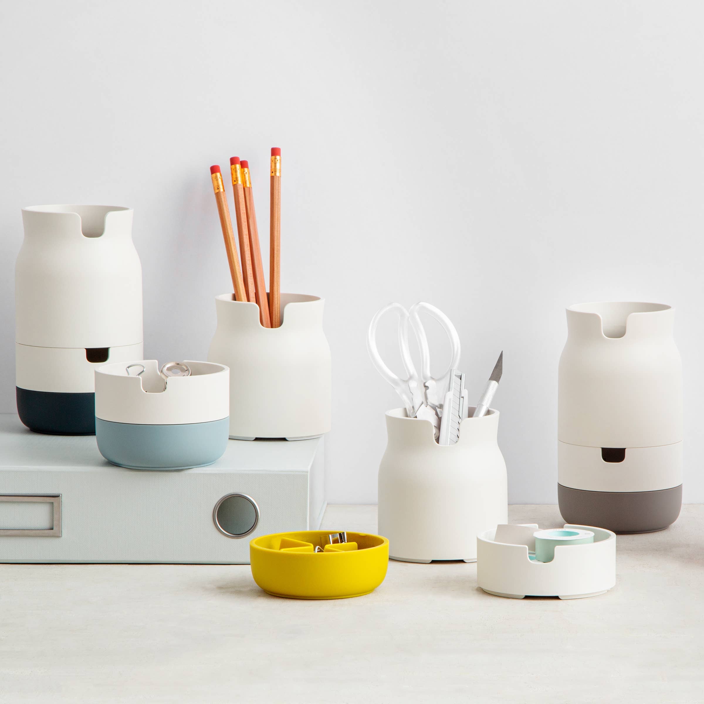 A collection of stackable porcelain-like organizers in various colors, containing pens and other desk items.