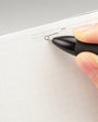 Hand holding a black pen over a white sheet of paper on a gray background