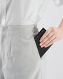 Person wearing light gray pants with a white shirt, holding a black wallet.