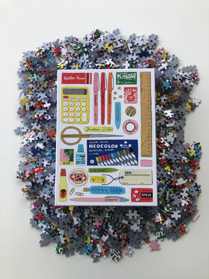 Pile of puzzle pieces with a packaging sheet featuring various tools and items on a white background