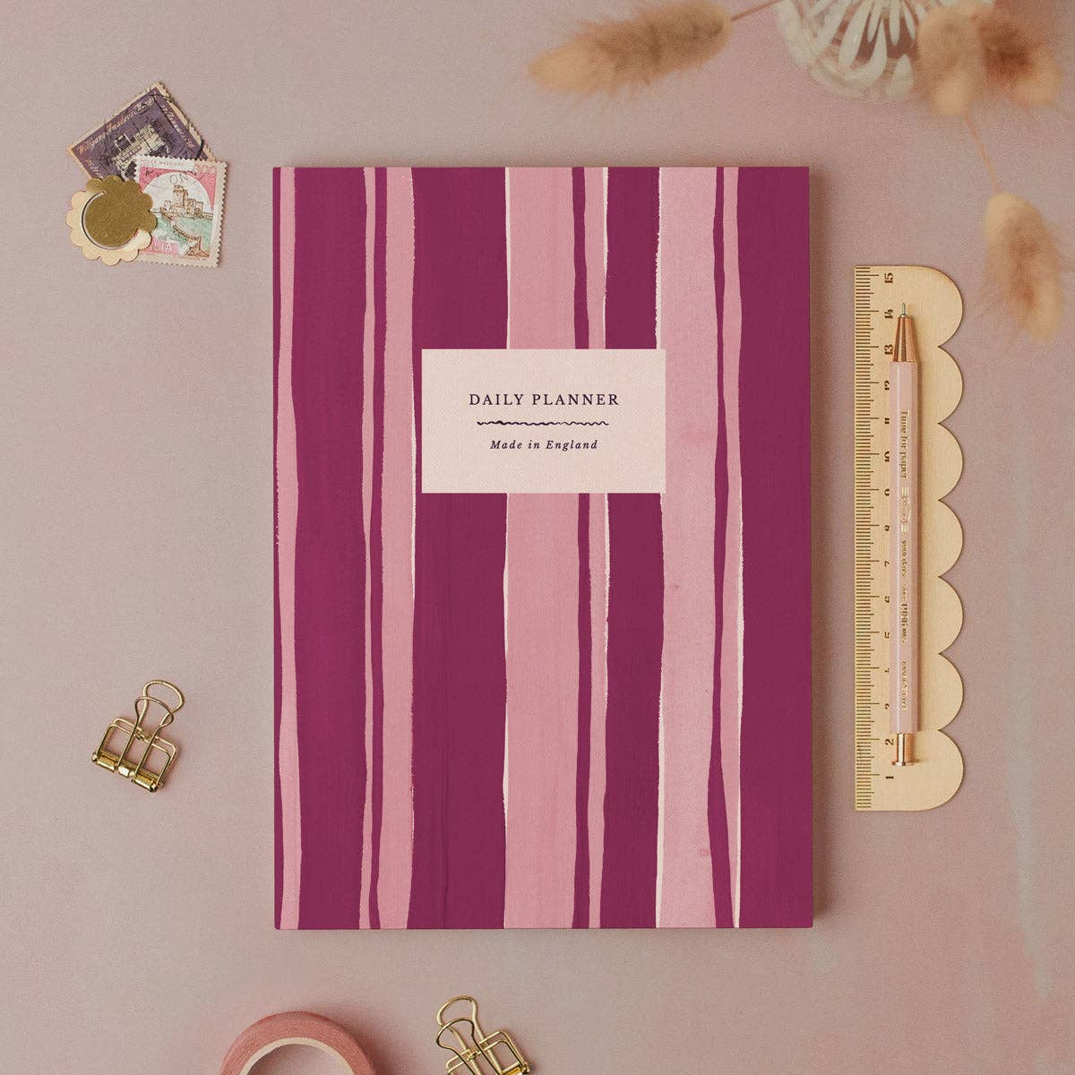 Purple and pink striped daily planner with stationery items on a pink background