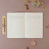 Open planner on a pink surface with decorative items