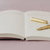 Open notebook with a gold pen on a light pink background