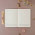 Open planner on a pink surface with decorative items