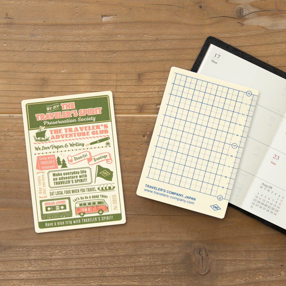 Notebook with grid page and promotional card on a wooden surface
