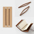 Brown leather notebook with open pages, cardboard holder, and wooden tongs on a white background