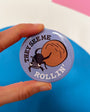 Button badge with text 'THEY SEE ME ROLLIN'' held by a hand against a colorful background