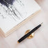 Black fountain pen with gold accents on a white surface next to a book with sketches.